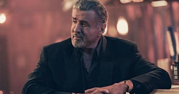 Sylvester Stallone sits with his arm against a table in a suit in The Tulsa King 