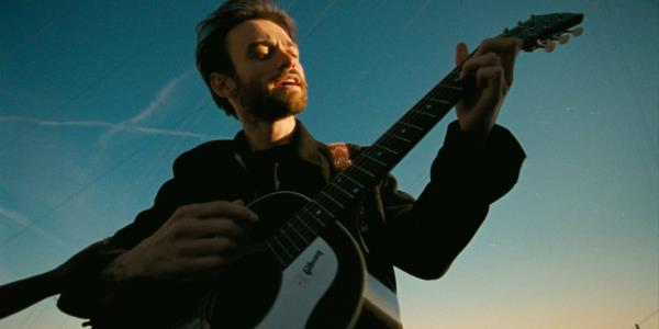 Casey playing his guitar and singing shot from a low angle in Dandelion