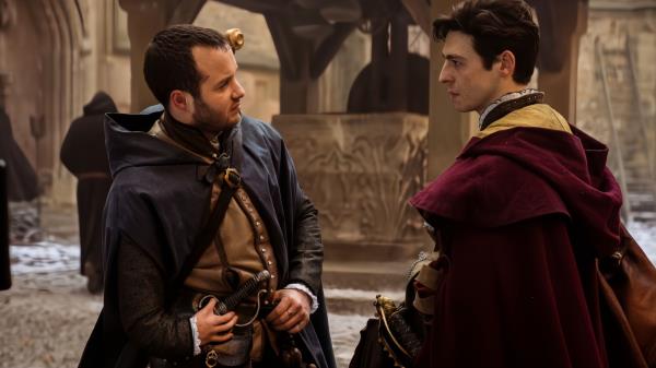 Arthur Hughes and Anthony Boyle standing in a courtyard together talking in Shardlake